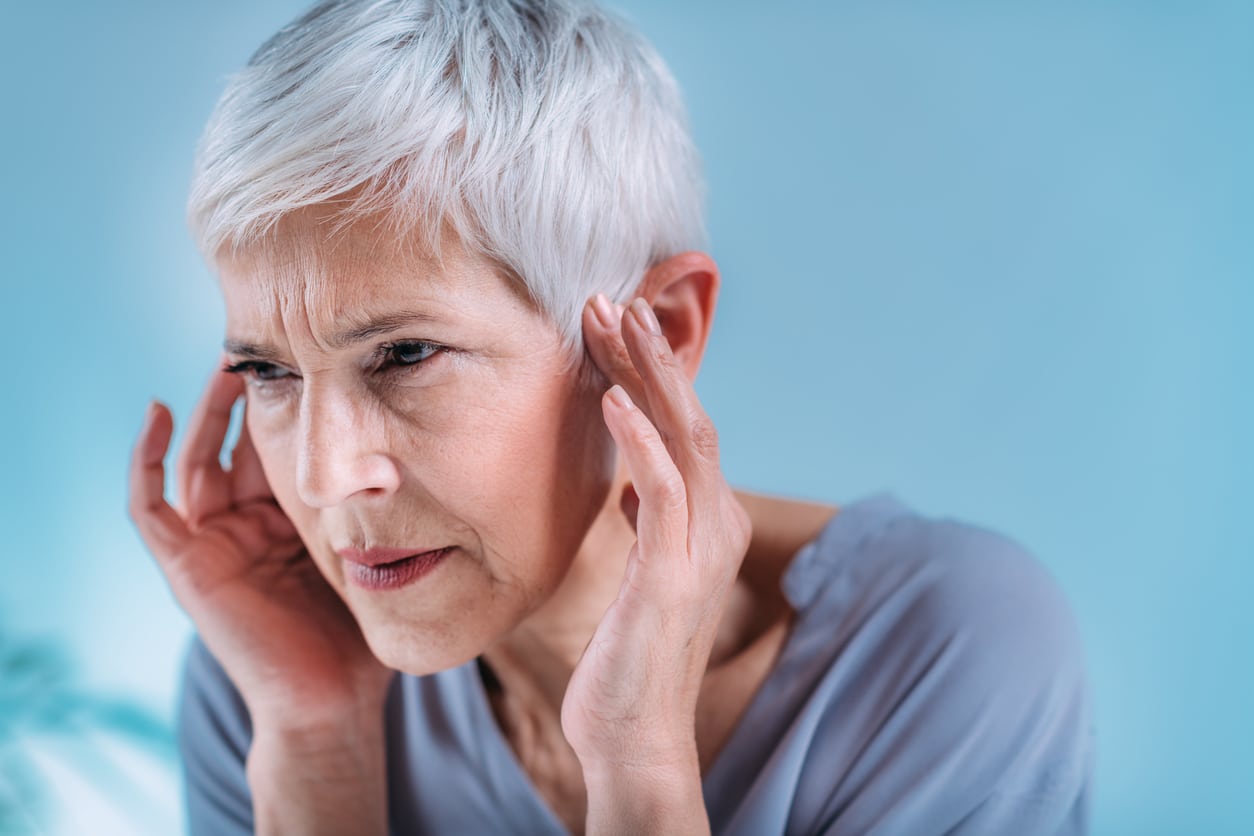 woman experiencing tinnitus symptoms Older woman holding temples and appearing to be in physical distress